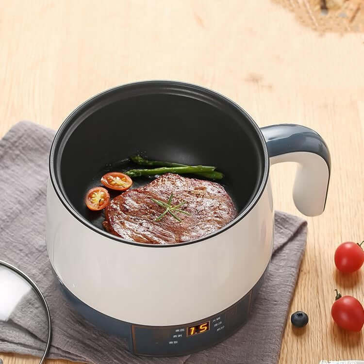 Electric cooking pot with steak, asparagus, and tomatoes on a wooden kitchen table