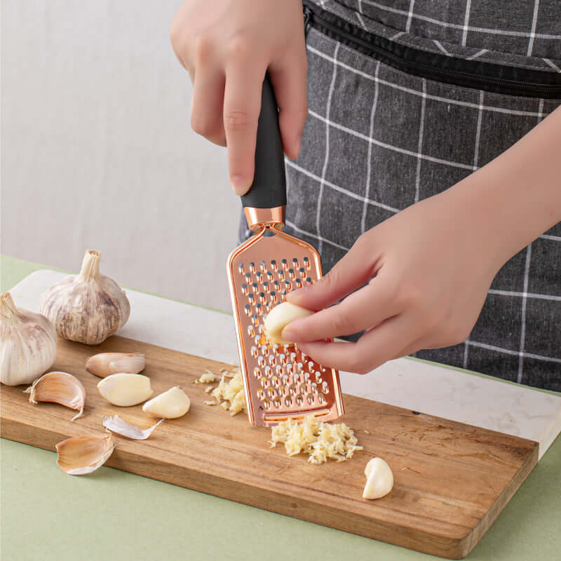 Hand grating fresh garlic on metal grater over wooden cutting board in kitchen setting