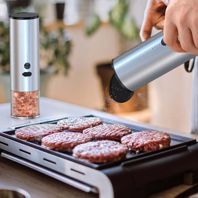 Electric salt and pepper grinder seasoning hamburger patties on indoor grill in modern kitchen