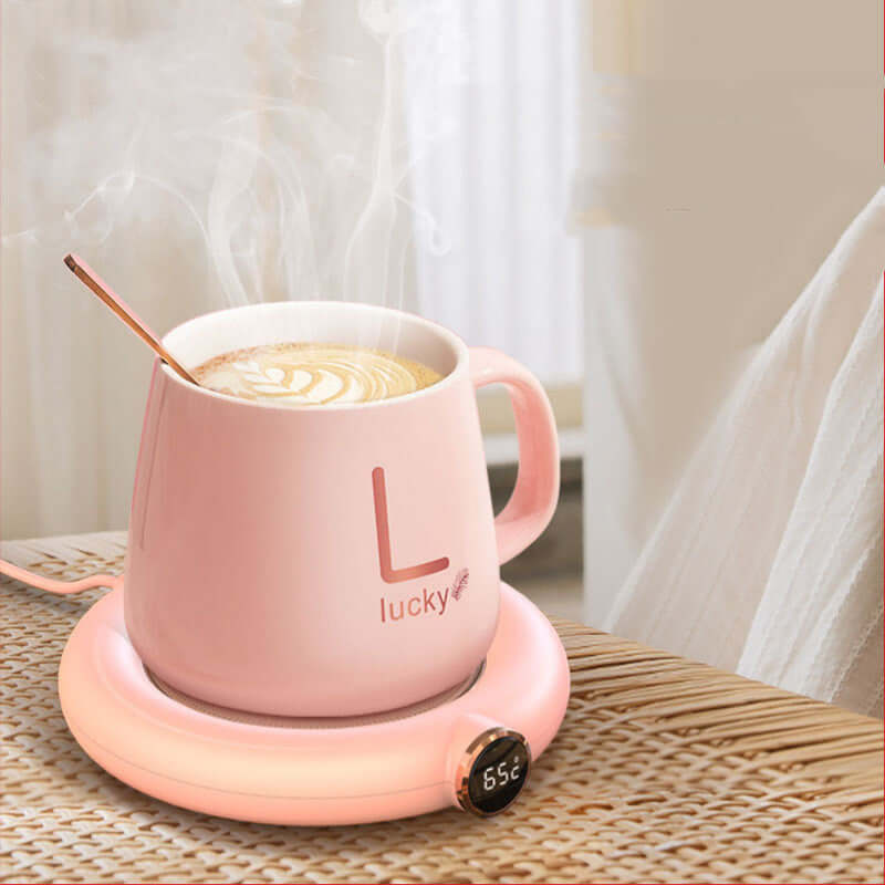 Pink ceramic mug on electric coffee warmer with temperature display, latte art inside