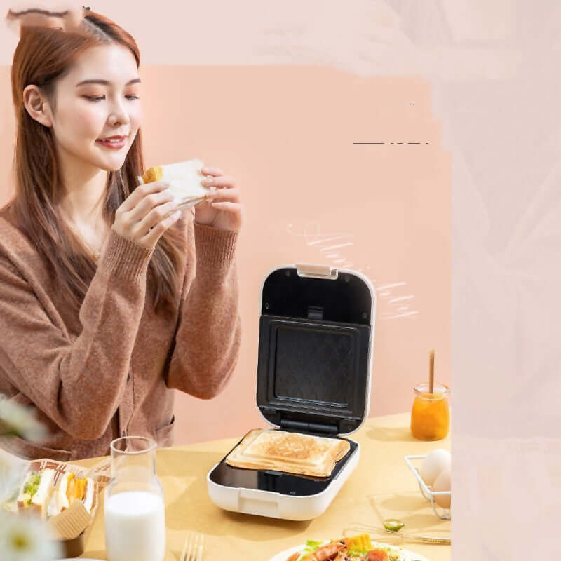 Woman using a sandwich maker with grilled sandwich, glass of milk, and breakfast foods on kitchen table
