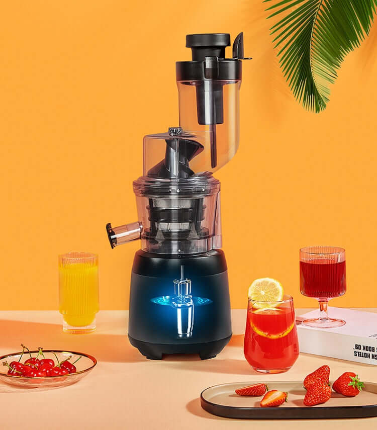 Electric juicer with fruit juices, strawberries, and cherries on a kitchen table