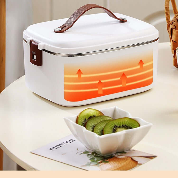 Electric heated lunch box with handle on kitchen table, kiwi slices in bowl nearby