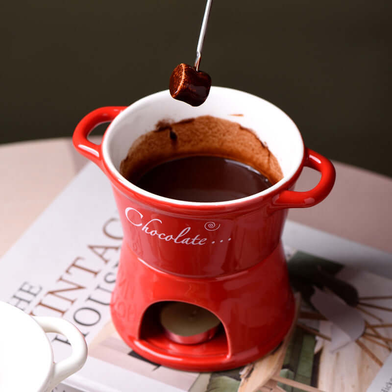 Red ceramic chocolate fondue pot with melted chocolate and fork dipping marshmallow, kitchen accessory