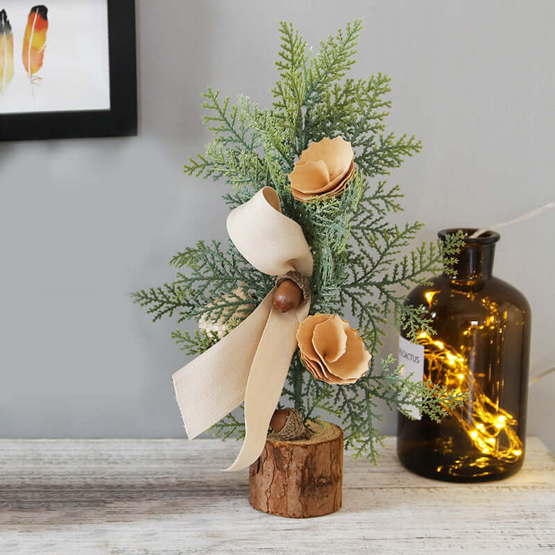 Artificial pine tree decoration with beige ribbon and flowers on wooden base, tabletop decor