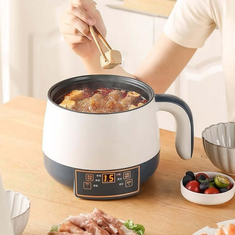 Electric hot pot cooking soup on kitchen table, person using chopsticks, food prep scene