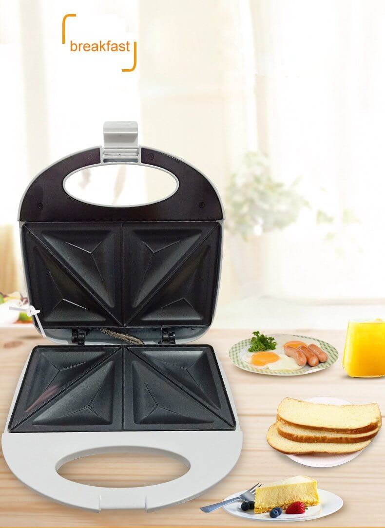 Open sandwich maker on kitchen table with bread, eggs, sausages, cake, and orange juice