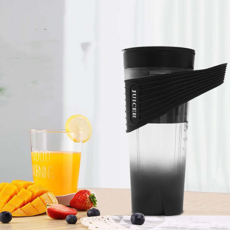 Handheld portable juicer with black lid and fruits, glass of orange juice on kitchen table