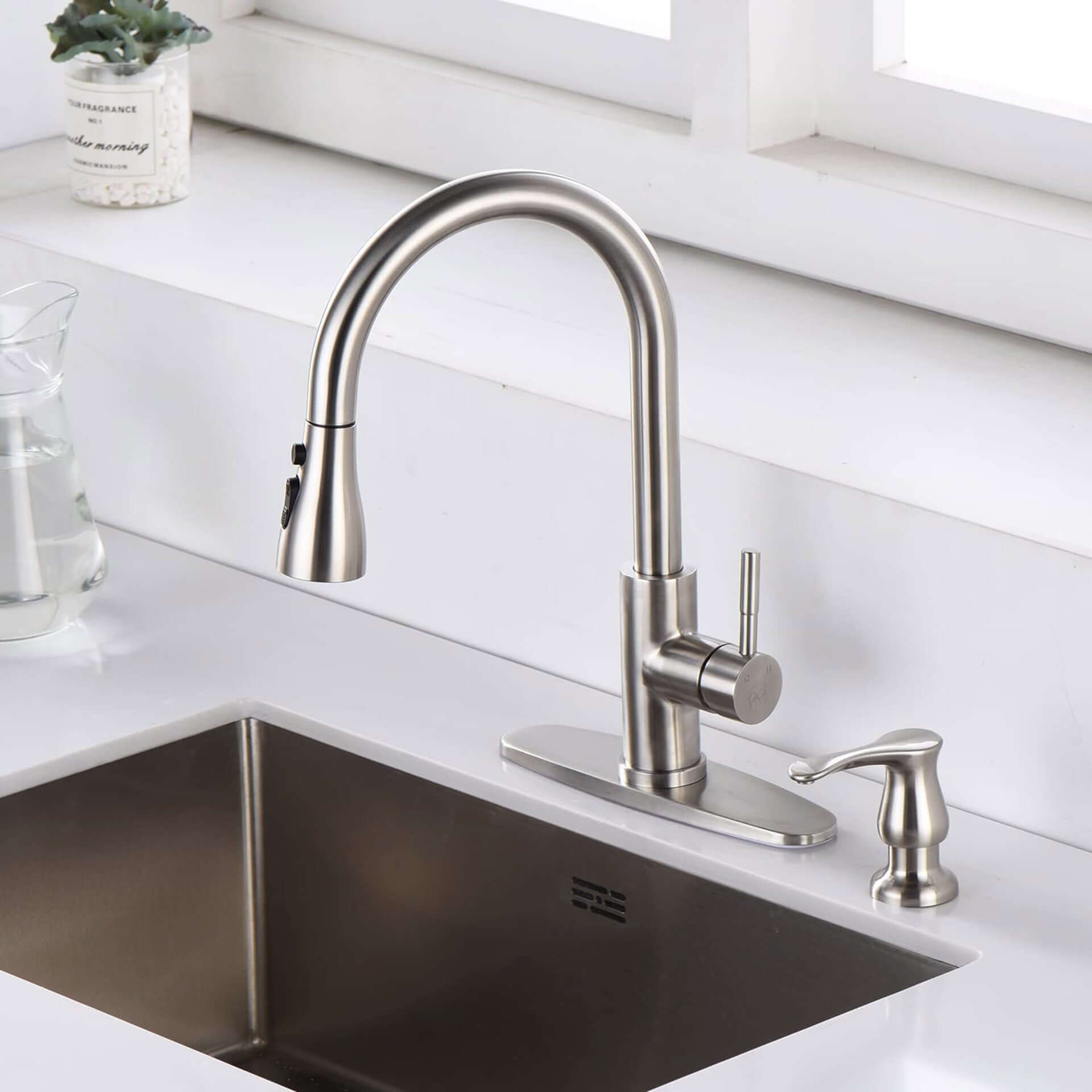 Stainless steel kitchen faucet with pull-down sprayer and soap dispenser on white countertop