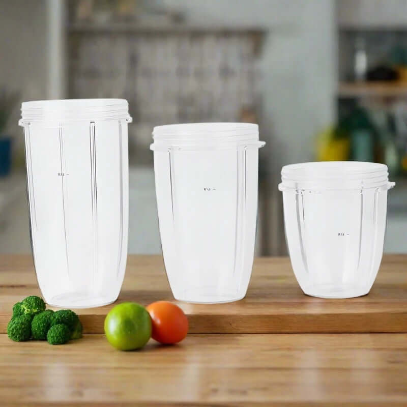 Set of three clear plastic blender cups on wooden kitchen counter with vegetables