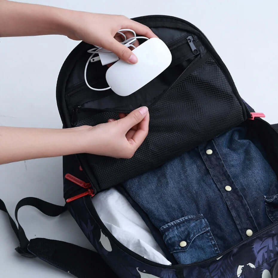 Person packing a charger into a black backpack with organized compartments and folded shirt