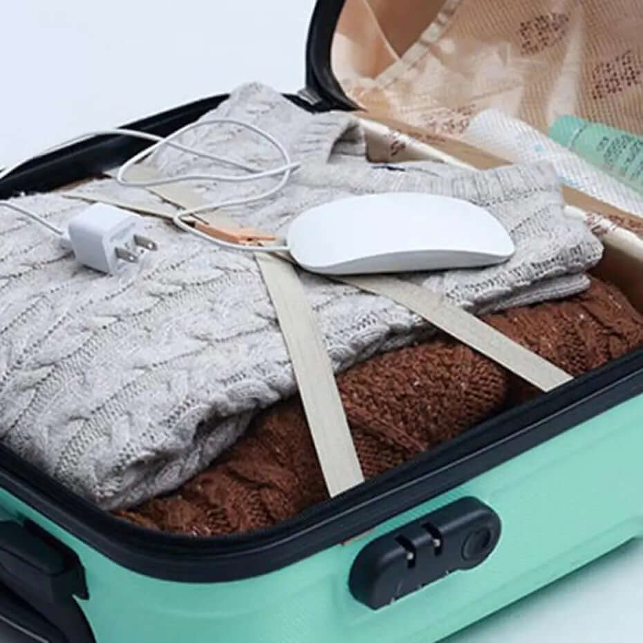 Open suitcase with folded sweaters, a computer mouse, and a charging cable neatly packed.