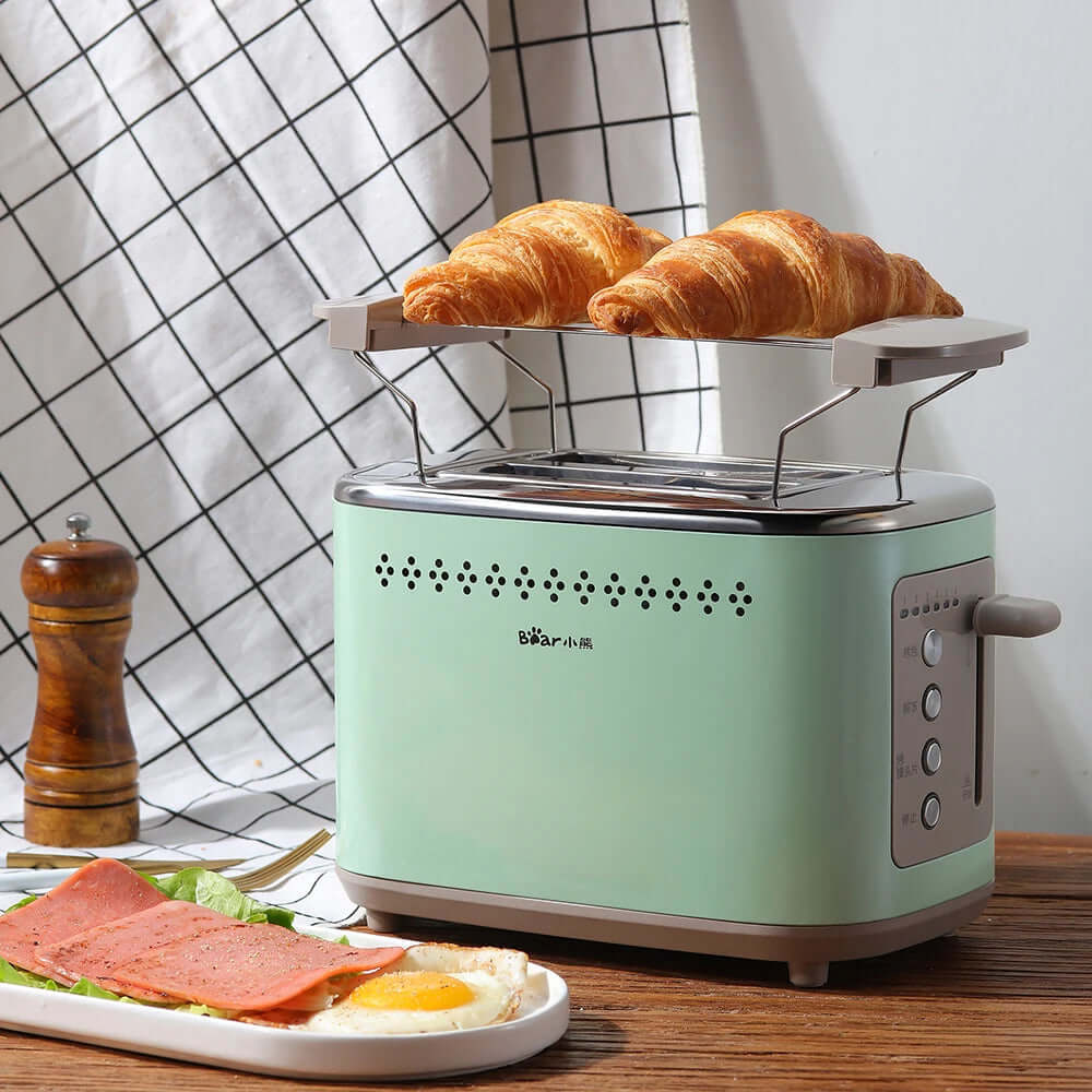 Mint green toaster with warming rack holding two croissants on kitchen counter