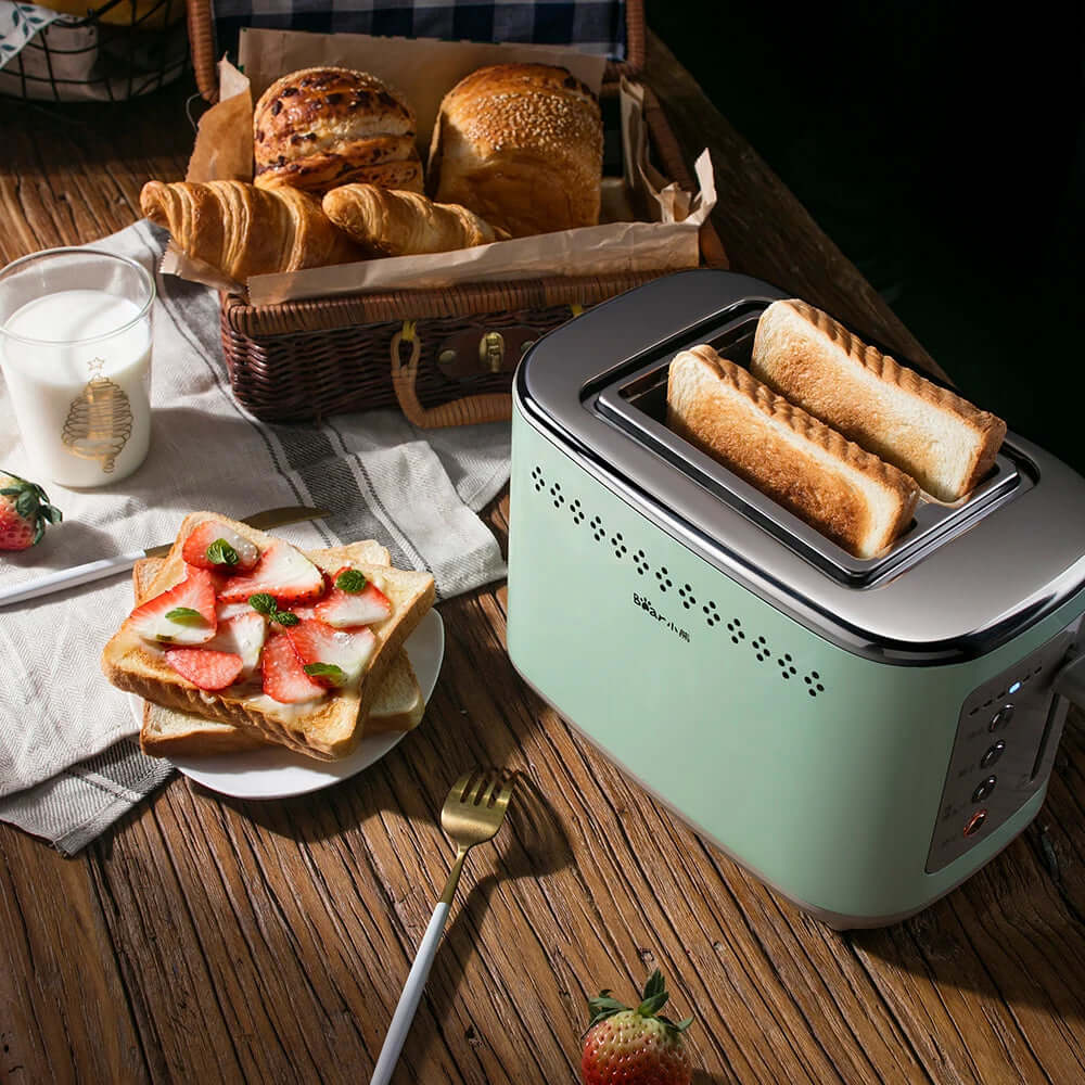 Green toaster with toasted bread, plate of strawberry toast, basket of bread, and glass of milk on wooden kitchen table