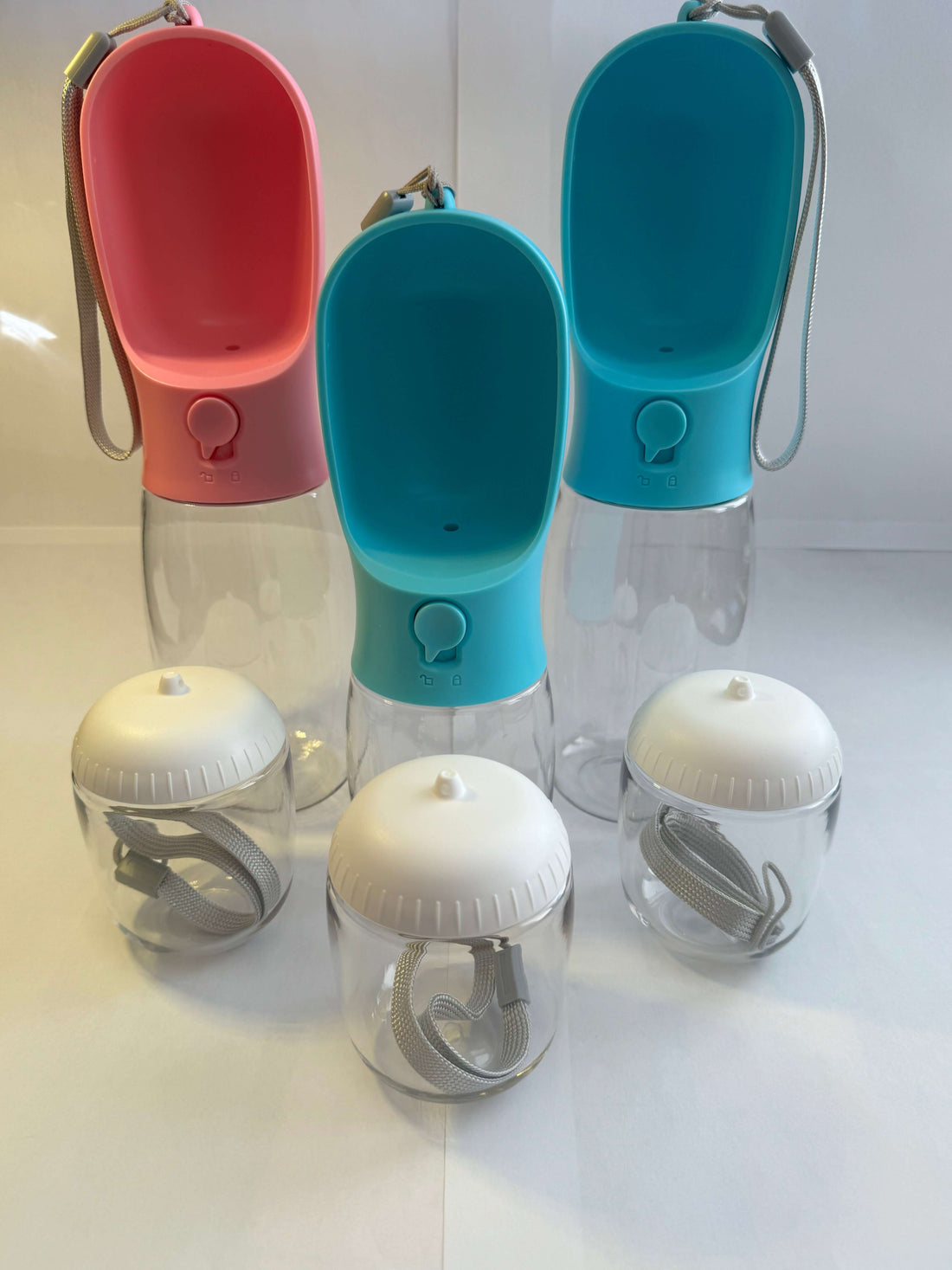 Colorful portable pet water bottles and small containers with carrying straps on white background