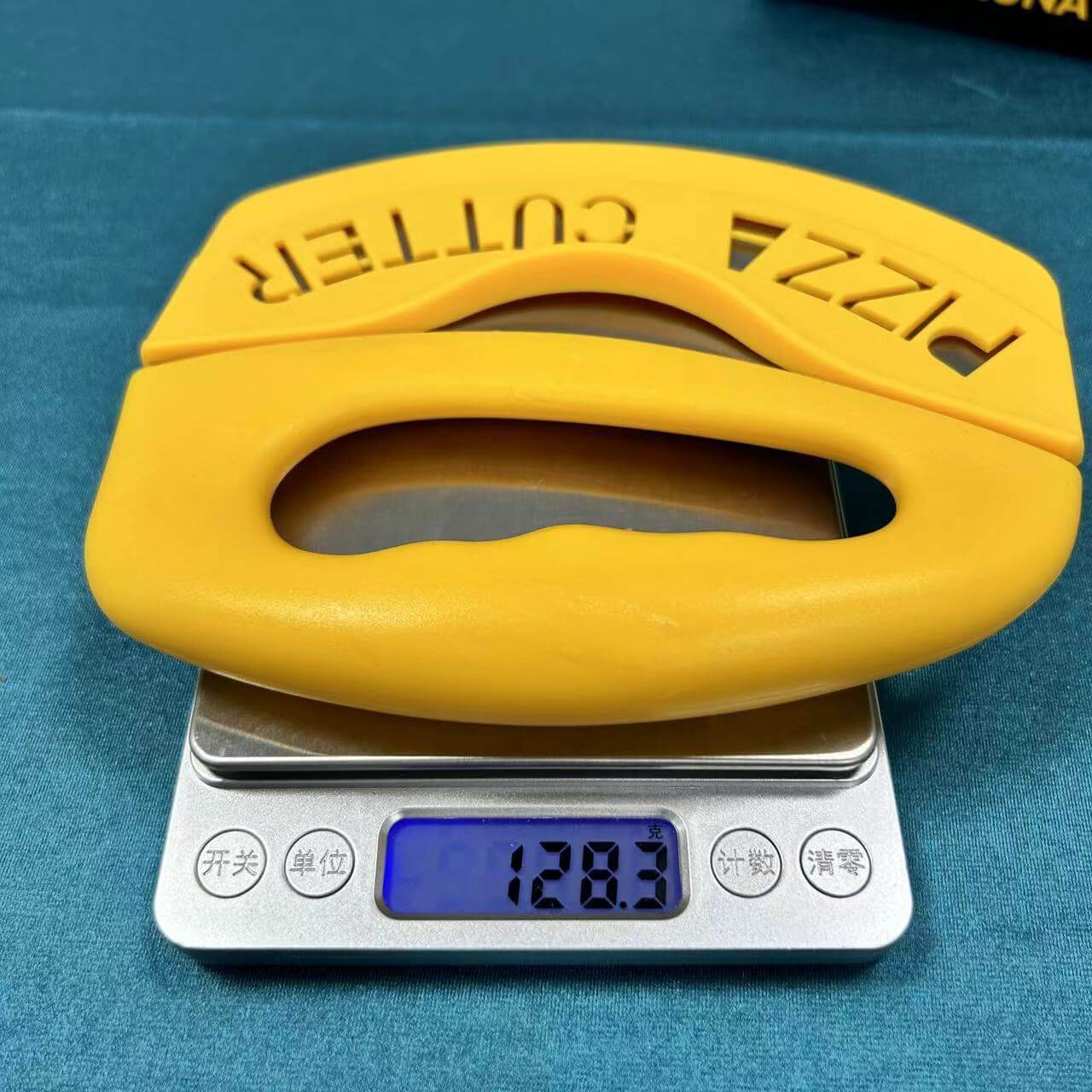 Yellow handheld pizza cutter with ergonomic handle on digital kitchen scale, weight 128.3g