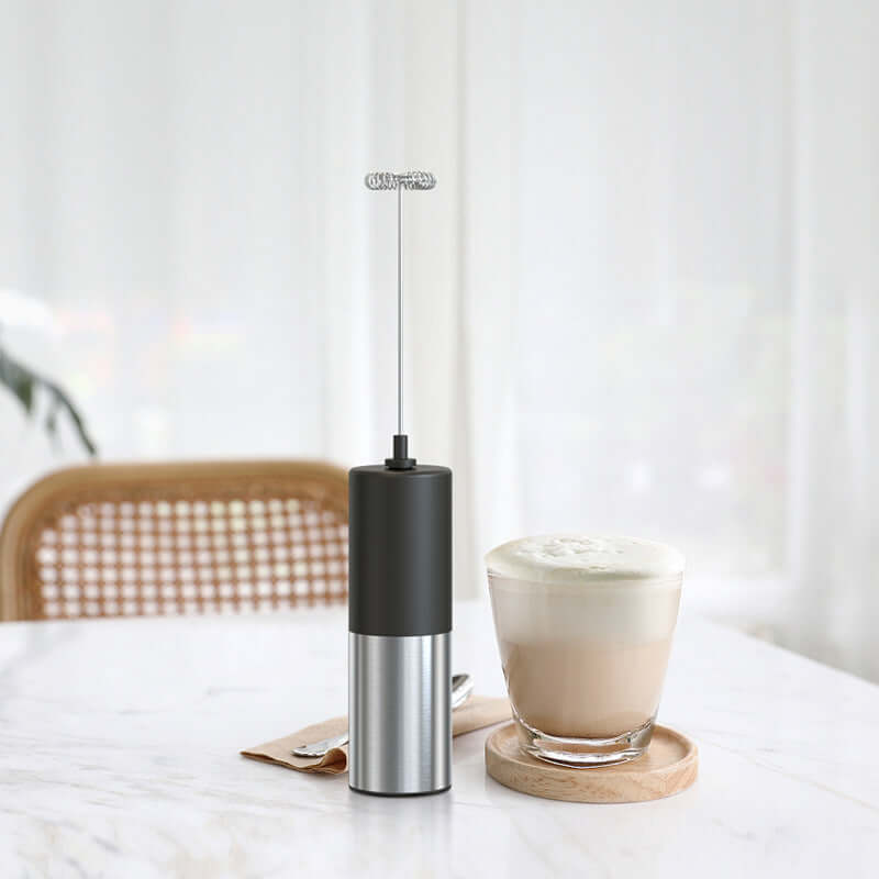 Electric milk frother and glass of frothed coffee on a kitchen table
