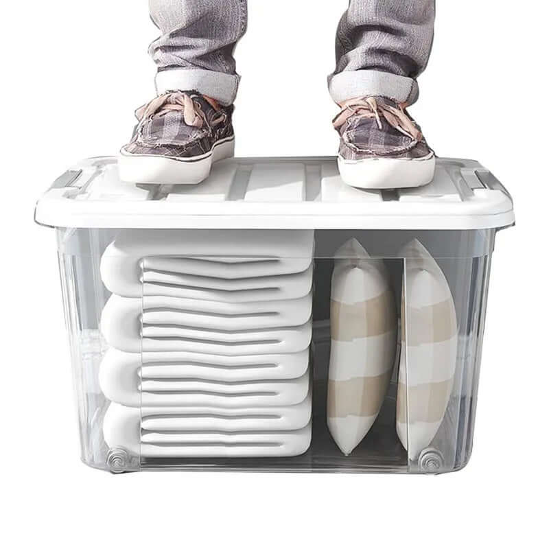 Clear plastic storage bin with white lid, stacked towels, and striped pillows, person standing on lid