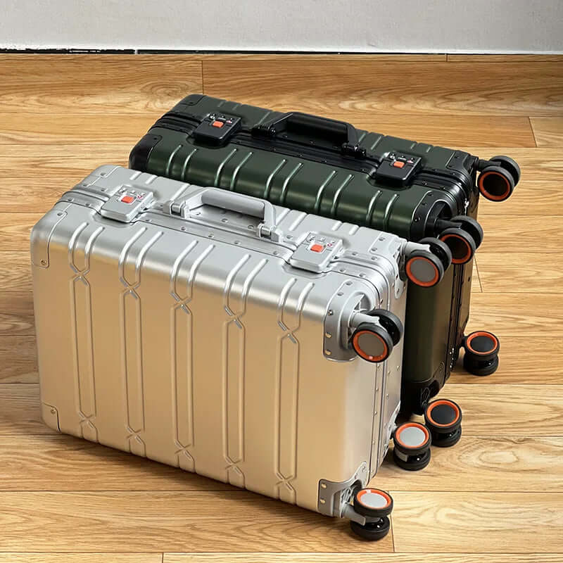 Two hard shell rolling suitcases, silver and green, with orange spinner wheels on wood floor