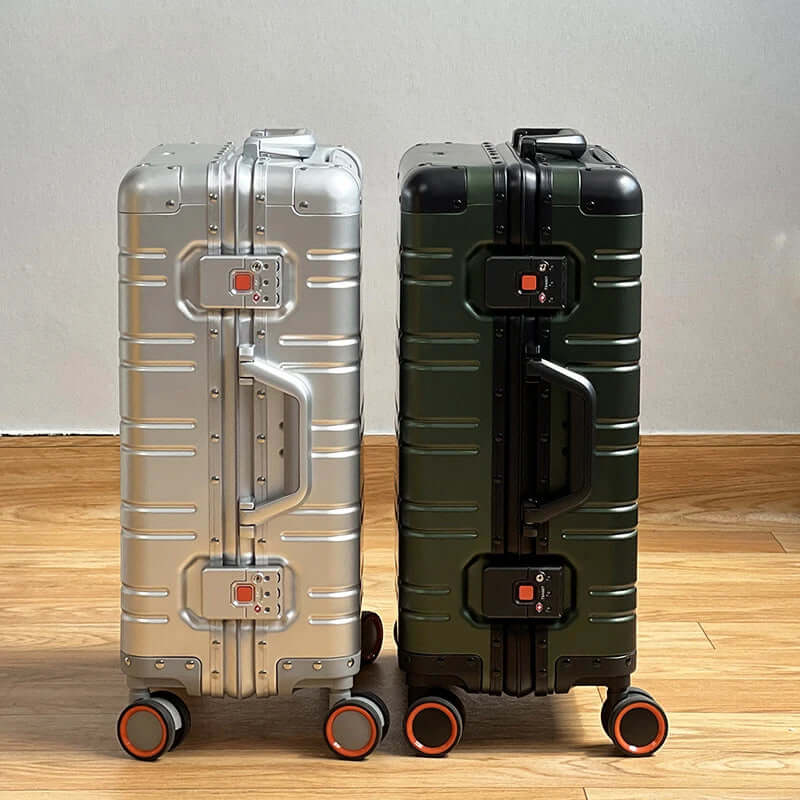 Two hard shell rolling suitcases, silver and green, side by side on a wooden floor