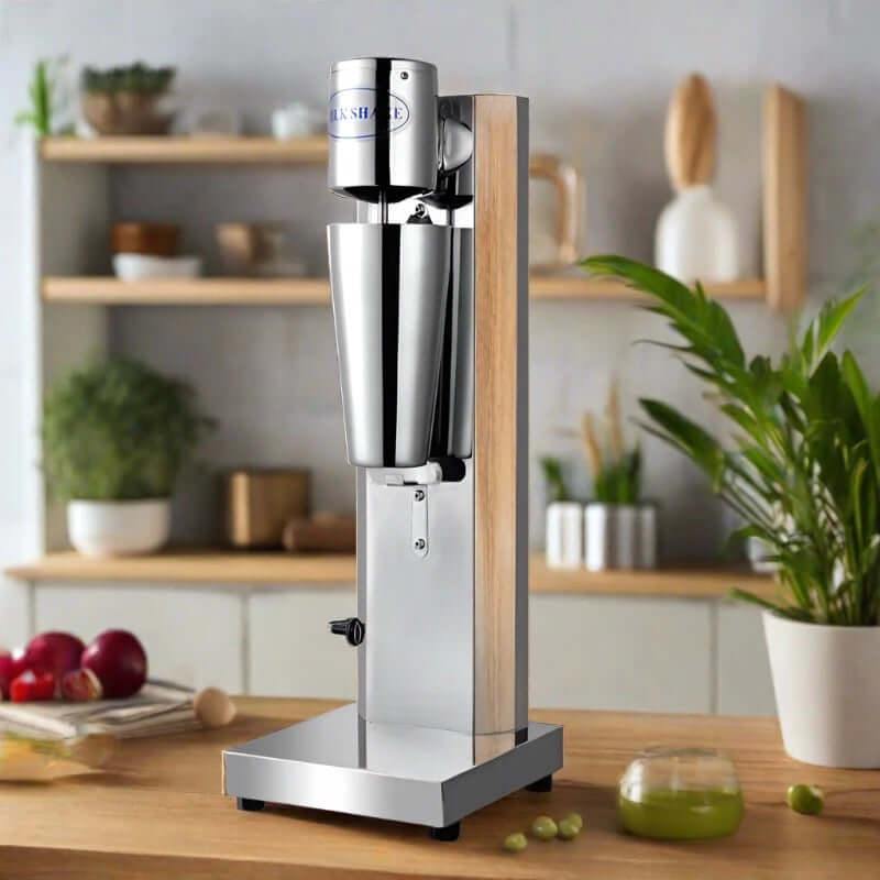 Stainless steel milkshake maker on kitchen counter with plants and utensils in background