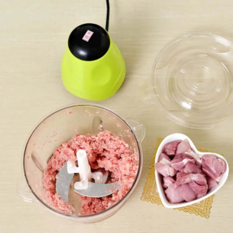 Electric meat grinder with green lid, minced meat in bowl, and raw meat in heart dish on table
