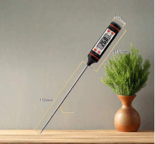 Digital kitchen thermometer with LCD display, stainless steel probe, and measurement dimensions on a wooden surface next to a potted herb.