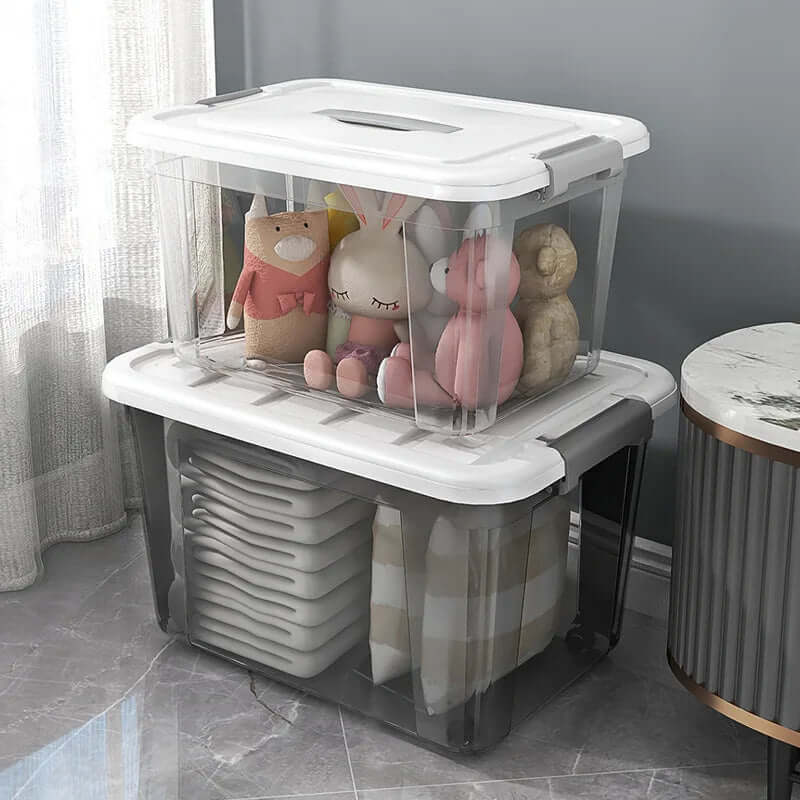 Clear plastic storage bins with white lids, holding stuffed animals and folded blankets, on a marble floor.