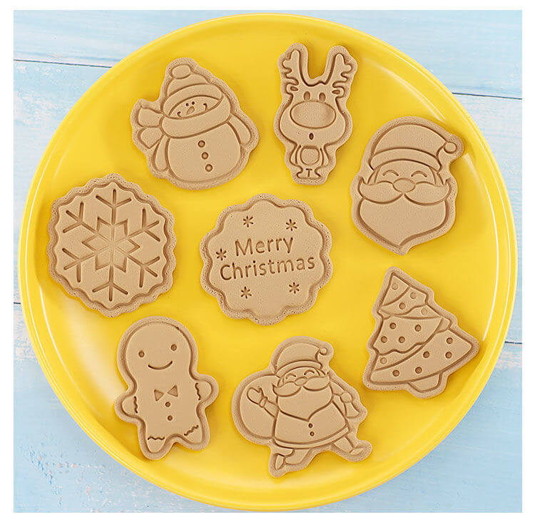 Christmas-themed cookie shapes on yellow plate, featuring snowman, gingerbread man, Santa, reindeer, tree, snowflake, and &