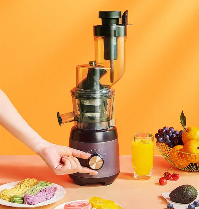 Electric juicer machine with control knob, surrounded by fresh fruit and juice on a kitchen counter