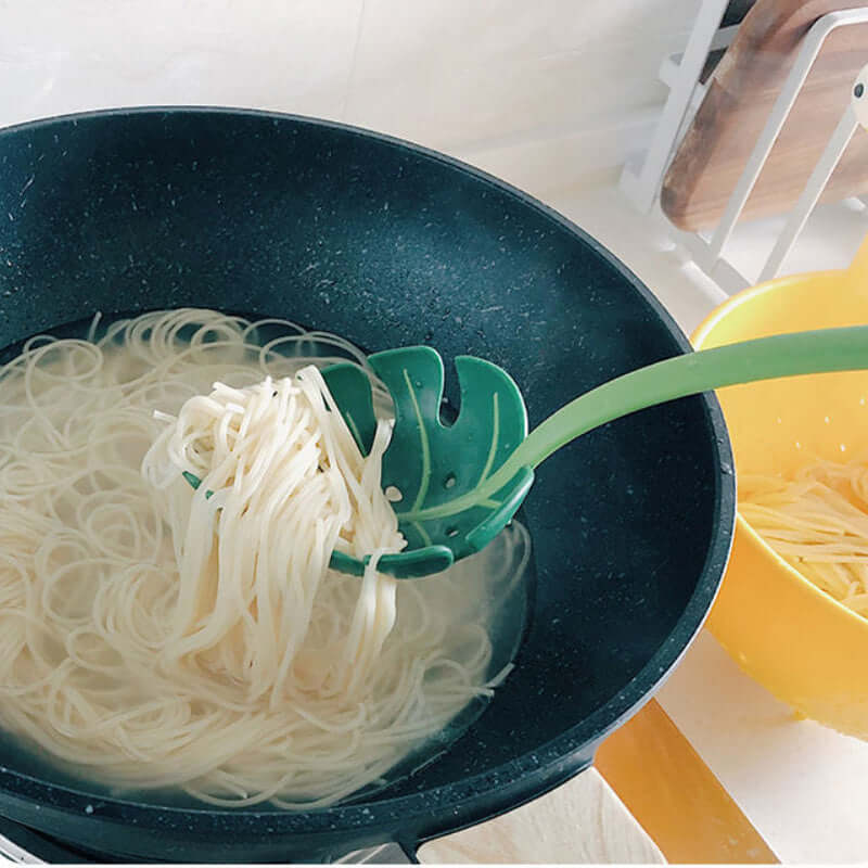 Green pasta spoon scooping boiled noodles from pot in modern kitchen