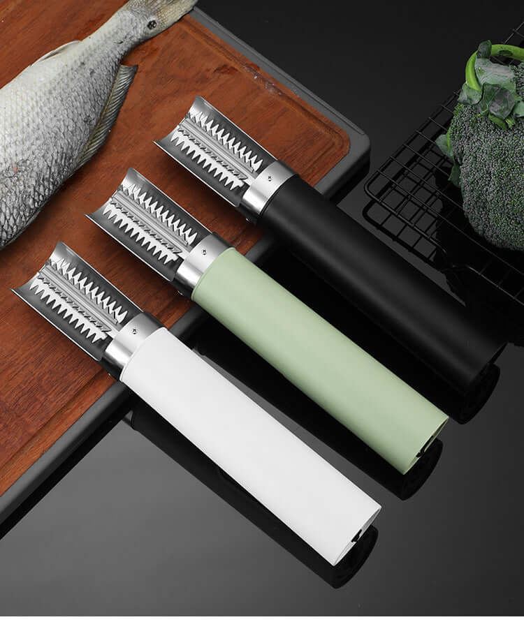 Three fish scalers with serrated metal blades and colored handles on kitchen counter near fish and broccoli