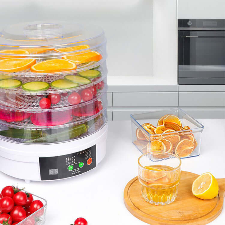 Electric food dehydrator with trays of sliced fruits and vegetables on a kitchen counter