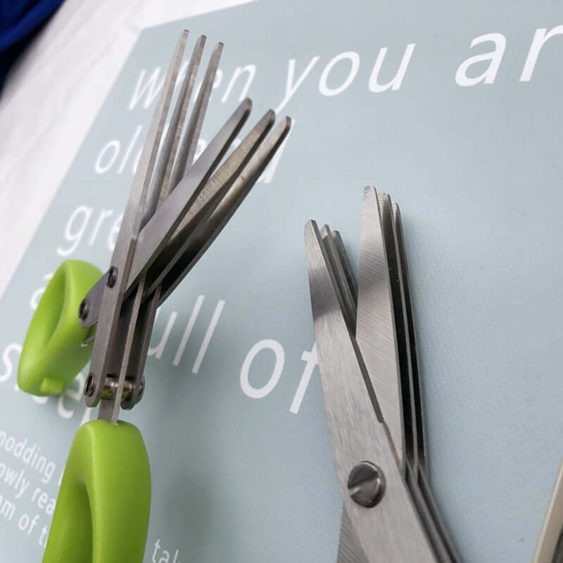 Multi-blade stainless steel kitchen herb scissors with green handles on a table