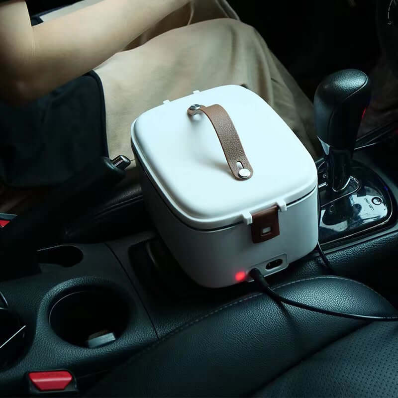Portable electric lunch box plugged in inside a car, positioned on the center console.