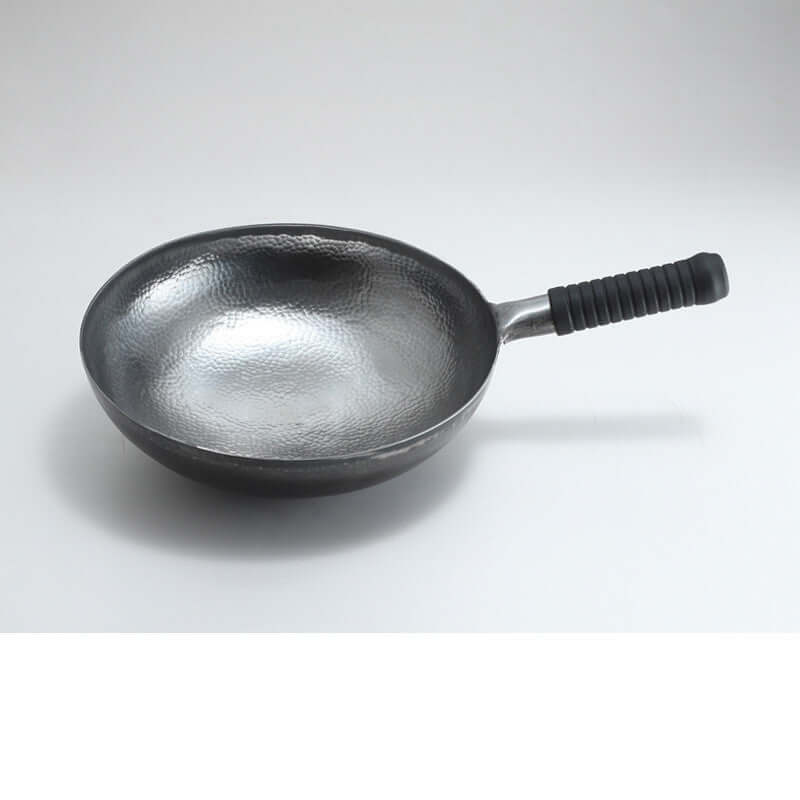 Hammered metal frying pan with black textured handle on white background