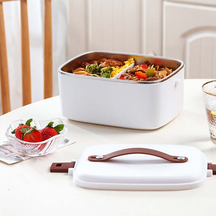 White bento lunch box with food compartments on kitchen table, lid and strawberries nearby