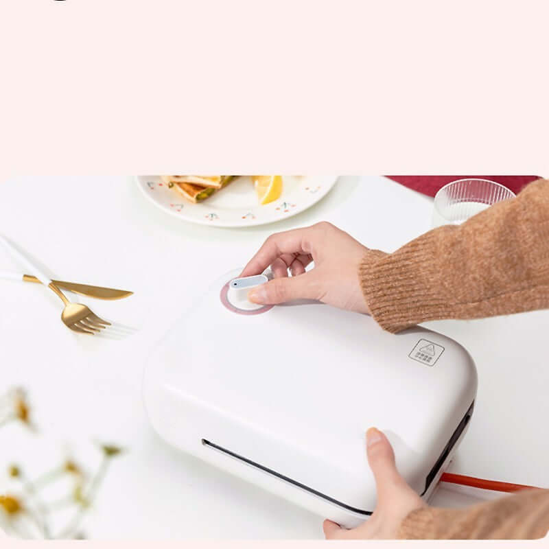Hand operating a compact white kitchen appliance on a countertop with utensils nearby