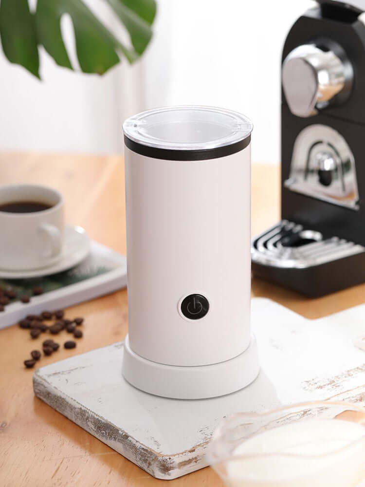 Electric milk frother for coffee drinks on kitchen counter with coffee maker and cup
