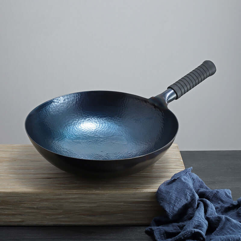 Hammered carbon steel wok with black handle on wooden board, kitchen accessories
