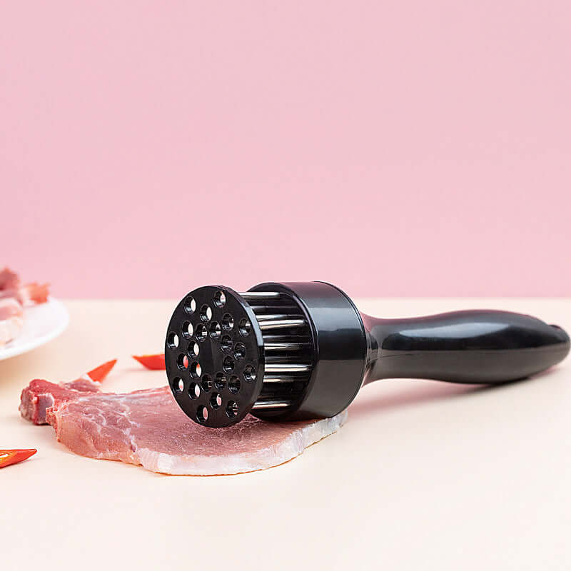 Meat tenderizer tool with black handle on raw steak, kitchen accessory on pink background