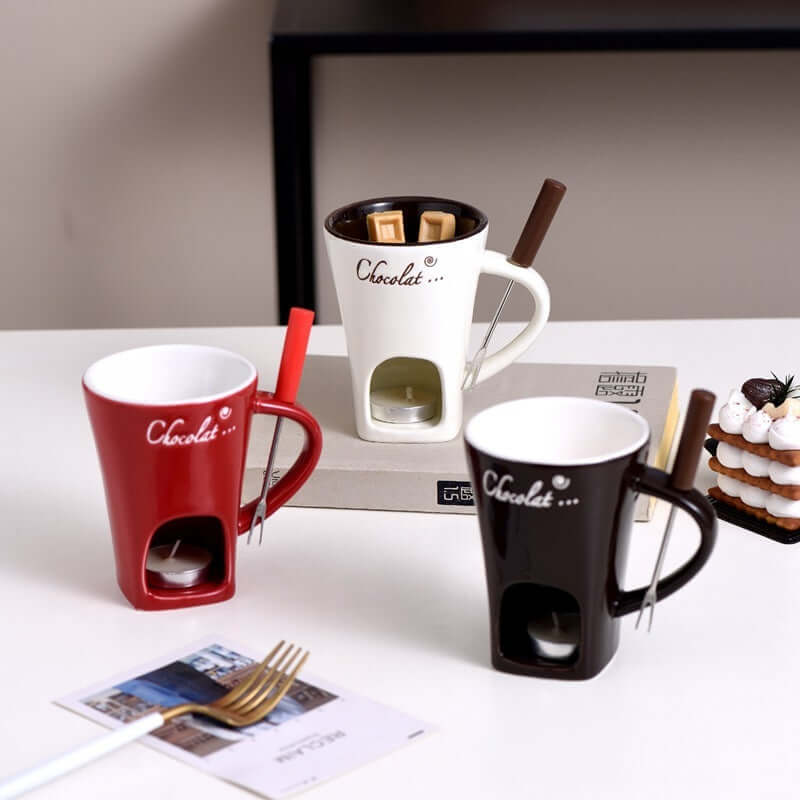 Ceramic fondue mugs with forks and candles for melting chocolate on a kitchen table.