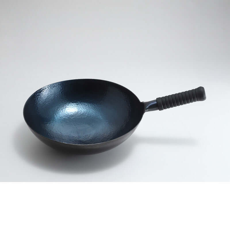 Hammered carbon steel wok with a textured nonstick interior and black heat-resistant handle on a white background