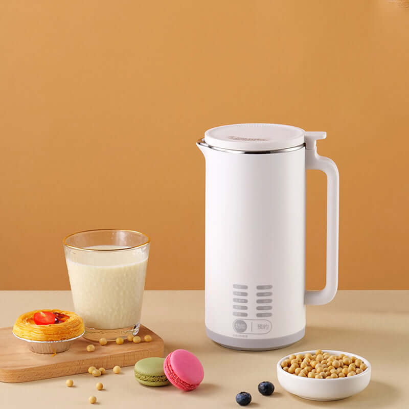 Modern white electric soy milk maker with glass of soy milk, pastry, macarons, and soybeans