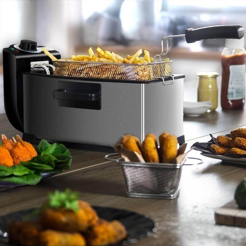 Electric deep fryer with basket of golden French fries on kitchen counter with fried snacks