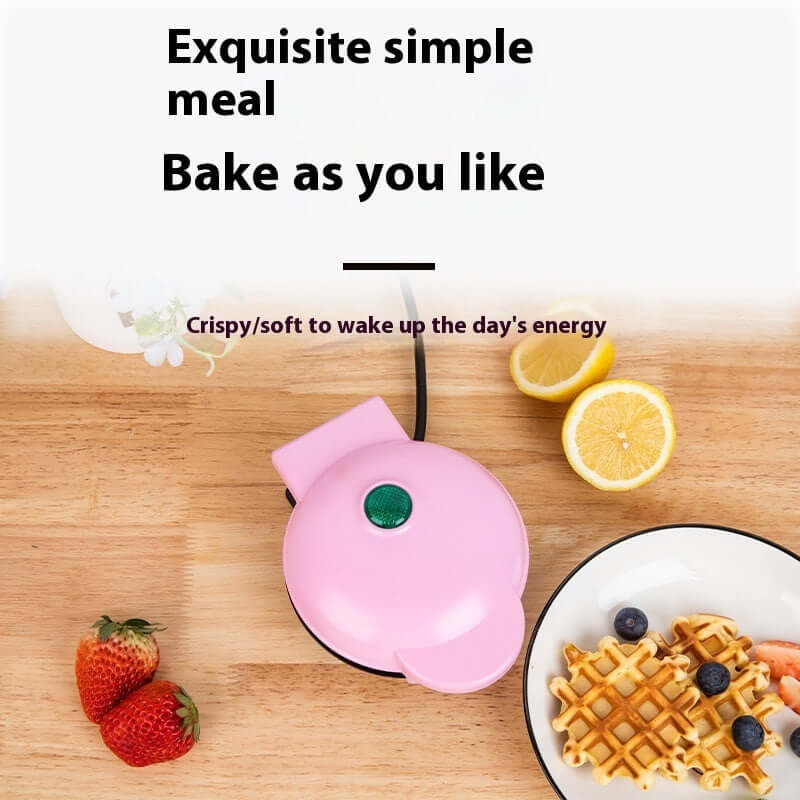 Pink mini waffle maker with waffles, strawberries, lemon and blueberries on wooden kitchen table