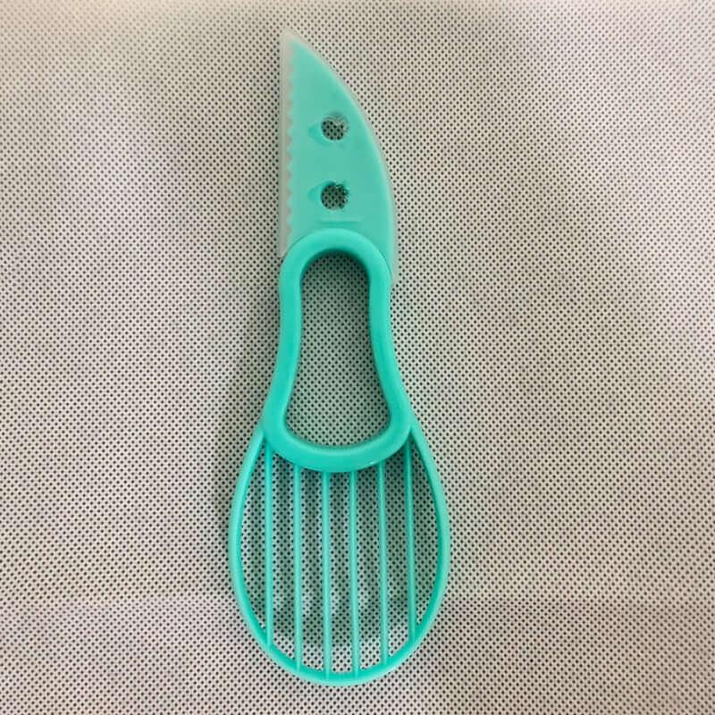 Aqua blue plastic avocado slicer and knife kitchen tool on a textured surface