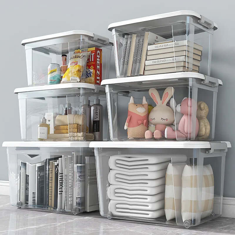 Stacked clear plastic storage bins with white lids holding books, snacks, toys, towels, and bottles