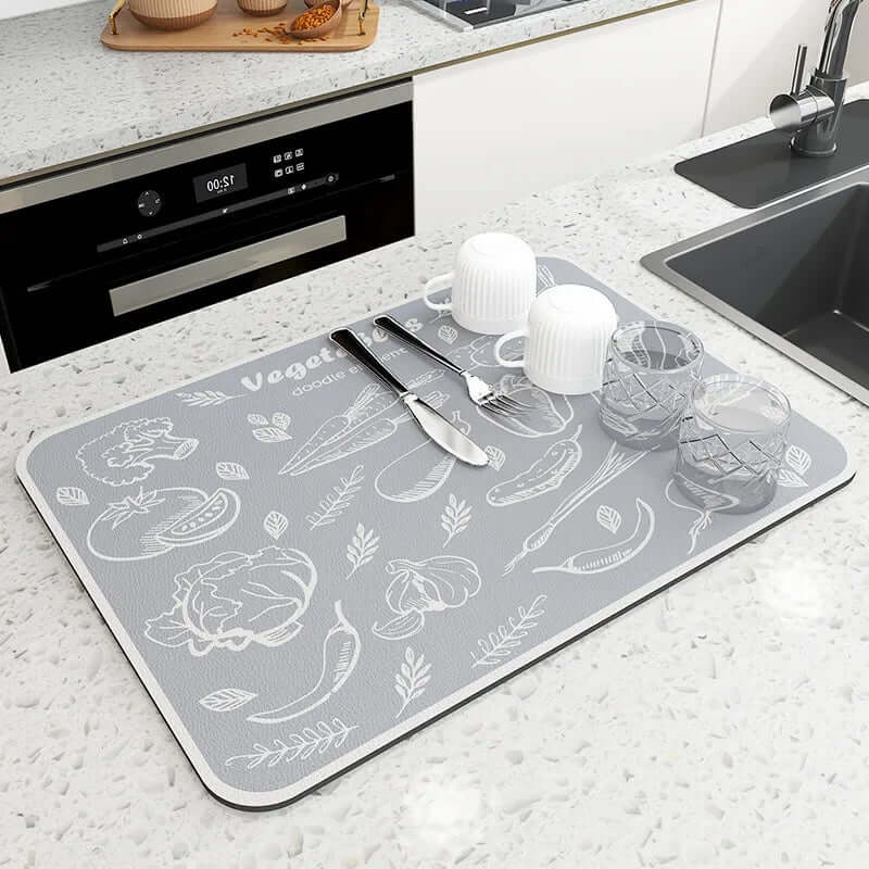 Gray kitchen drying mat with vegetable illustrations on countertop, holding cups and utensils