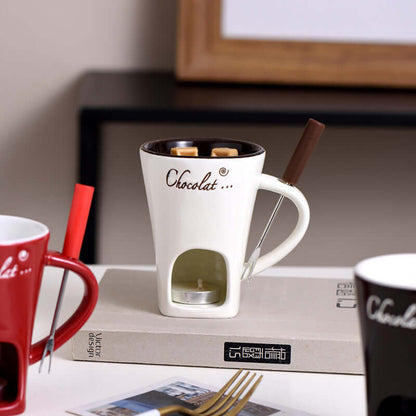 Ceramic fondue mug with chocolate, tealight warmer, and fondue fork on a table